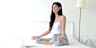 美丽的年轻女子在白色房间的床上练习瑜伽