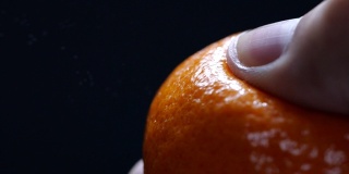 在黑色背景的慢动作中挤压橘子皮。健康食品。特写镜头。宏