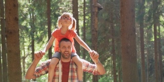 在森林里，父亲背着女儿的正面视图。父亲抱着女儿在森林小径上徒步旅行。父亲和女儿一起在森林小径远足