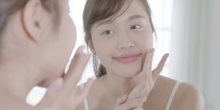 美丽的年轻亚洲女性愉快地应用霜或乳液与保湿面部，美丽的亚洲女孩应用护肤触摸面部化妆，健康和健康的概念。