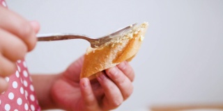 孩子的手把大蒜奶油涂在切片的法国面包上。