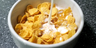 在碗中倒入牛奶和干玉米片准备早餐。