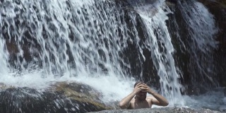 男鞋踩在山间瀑布的石头上。游客在山间瀑布中沐浴。英俊的男子在热带雨林享受新鲜的山河