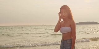 在沙滩上跑步的亚洲女人。年轻快乐的女性在比基尼放松和有趣的热带海时，日落而度假，夏季旅行的概念。慢动作镜头。