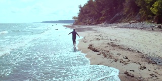 鸟瞰图的年轻潮人沿着野生海滩奔跑。在海边奔跑的人。运行在水面上。野生自然。4 k UHD。天线。人在天空下的沙滩上出海。