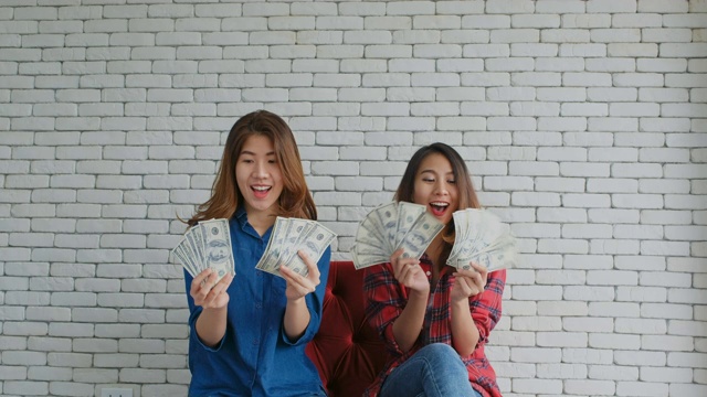 快乐的两个年轻的亚洲女人拿着美元钞票兴奋地吐出人和商业财务