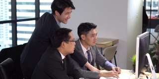 一组快乐的年轻商人团队一起工作与显示器电脑或屏幕上讨论信息在办公室。老板和助理或秘书讨论在Windows玻璃背景