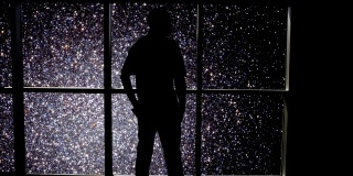 在这个抽象概念中，一个人的剪影站在窗前，俯瞰着一个星团。
