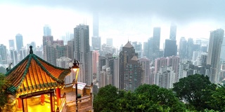 4K时间跨度的摩天大楼和城市景观在多云大雾的早晨日出从维多利亚山顶海港，香港。在中国香港的摩天大楼建筑工业上空移动云的高角度鸟瞰图。