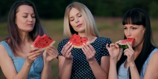 日落时分，三个年轻迷人的女性朋友在吃着西瓜，面带微笑。