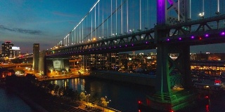 照明费城市中心，本杰明富兰克林桥和码头在老城在特拉华河晚上。无人机视频与下降的摄像机运动。