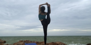 4k/年轻的亚洲苗条女子瑜伽在日落的海滩上，日出的背景。健身、运动、瑜伽和健康理念。