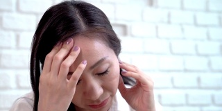 亚洲中年妇女正用手捧着头，头疼得无可救药。