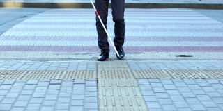 盲人男性用白色手杖过马路，用触觉瓷砖导航城市