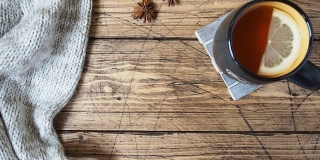 秋季概念温馨的家。木桌上放着柠檬茶和围巾。秋天的橡树叶落在桌子上。