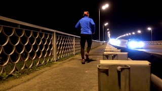 晚上在桥边慢跑的运动员。一个穿着运动服的男人在晚上跑步。男正在健身，车路过。傍晚沿着高速公路慢跑。视频素材模板下载
