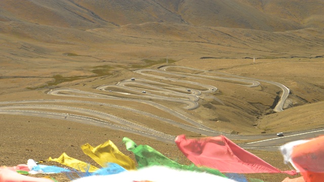 近距离观察:彩色的经幡飘扬在瓜拉山口蜿蜒的道路上