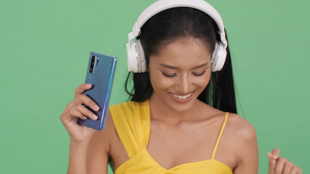 亚洲美女听音乐在线和幸福的情绪微笑。女人戴着耳机，拿着智能手机。美的概念，时尚和音乐体验。