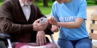 女志愿者教坐在轮椅上的残疾老人如何使用手机