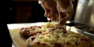 烹饪披萨。厨师把磨碎的奶酪撒在培根和生面团上。慢动作视频，100帧/秒