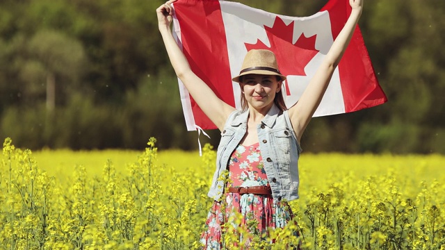 夏天，一位成年妇女举着加拿大国旗在油菜籽地里跳舞。