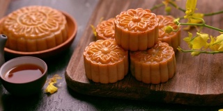 美丽的月饼在木托盘与茶和花在黑石板背景。中国传统的中秋节观念。