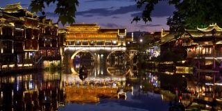中国凤凰。傍晚镇上的七彩映照在河上。一条船在河上航行。两岸的人们都玩得很开心。全景镜头,UHD