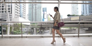 女商人使用智能手机在城市中步行上班，早上通勤上班