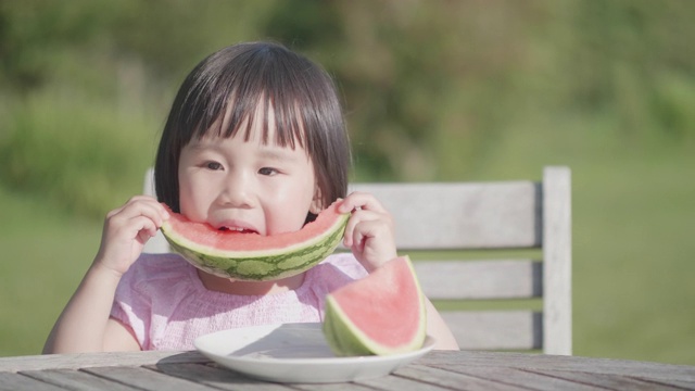 蹒跚学步的小女孩在夏天的家花园里吃西瓜