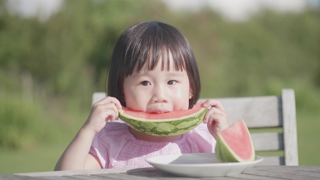 蹒跚学步的小女孩在夏天的家花园里吃西瓜