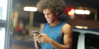 一个年轻的黑人在夜色中微笑着看手机短信