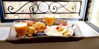 窗台上的法式早餐托盘。羊角面包，奶酪，果汁，果酱，圣女果和法棍面包