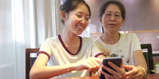 亚洲家庭年轻的青少年和母亲度假放松使用数字平板电脑和智能手机在家里做作业，放松与在线游戏和在社交网络上的短信