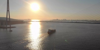 航拍一艘大型集装箱船通过海峡进入港口，上面有一座巨大的电缆桥