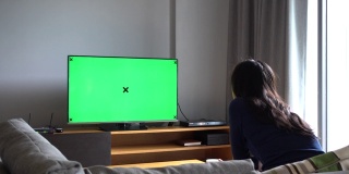 亚洲妇女看电视与绿色屏幕，拍摄背后的模特肩膀