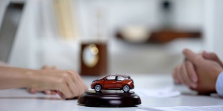汽车玩具在桌子上，女人签署车辆购买或保险的背景