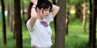 美丽的中国女孩在白色衬衫将她的黑色长发扎成马尾辫在阳光明媚的夏日森林，美丽，生活方式概念，4k镜头，慢动作。