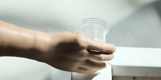 一个残疾人拿着一个塑料杯子喝水。一只义肢举起一杯水。独立完整的生活与假肢