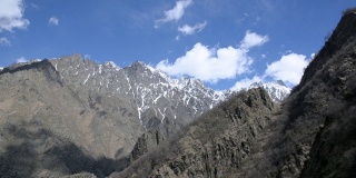 轻盈的白云漂浮在高高的、崎岖的山顶上，山上还残留着积雪。高加索地区。格鲁吉亚。