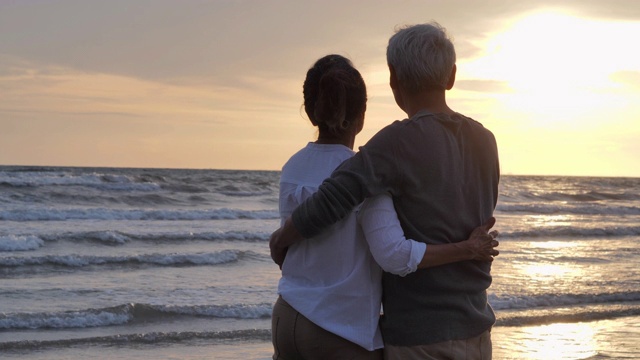 一对老年夫妇在海边休息。老年假期，假期退休度假概念，快乐成熟的退休夫妇享受美丽的日落在海滩，老年夫妇在慢镜头。假期——iStock