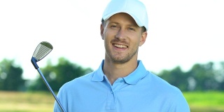 微笑的高尔夫球手拿着铁棒对着相机摆姿势，爱好，休闲活动