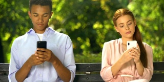 男女青少年坐在长椅上，用智能手机聊天，问题