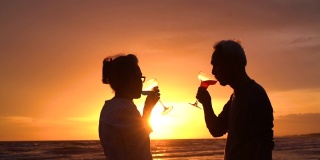 剪影亚洲夫妇老年人退休放松在海滩和喝葡萄酒或香槟，拥抱在日落蜜月家庭一起幸福的人的生活方式，慢镜头