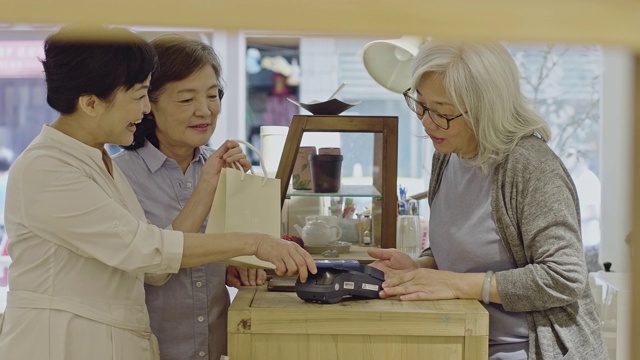 两名亚洲妇女在商店用手机付款的慢动作视频