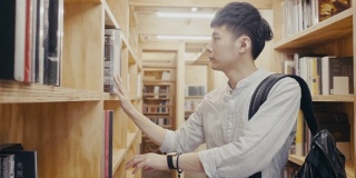 年轻的亚洲男大学生在图书馆找书(慢镜头)