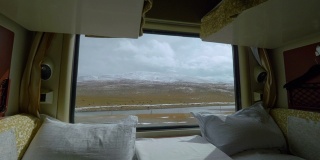 特写:从一辆卧铺火车的窗口拍摄的西藏平原风景。
