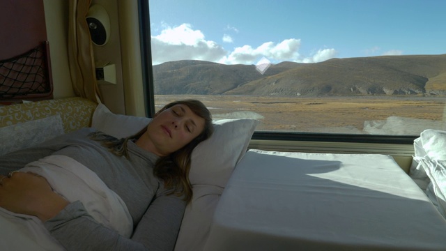 特写:一名年轻女子在穿越西藏的火车上睡在柔软的床上。