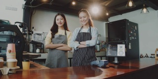 两名年轻美丽的亚洲女咖啡师穿着围裙，微笑着站在咖啡馆的吧台边交谈。咖啡店和小型咖啡店的概念。缓慢的运动。