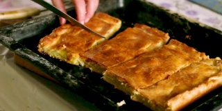 一个女人用带边的烤盘上的刀切刚烤好的、热气腾腾的奶酪土豆馅饼。