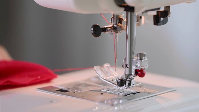 女裁缝的双手在缝纫机上缝红衣服直缝。
